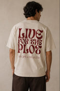 A man modelling a cream-colored short-sleeve t-shirt. The back view features a large red graphic reading 'LIVE FOR THE PLOT' and the Recipe for Disaster logo underneath