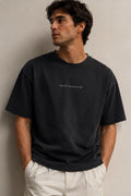 A man wearing an oversized black short-sleeve t-shirt with 'RECIPE FOR DISASTER' printed in white on the chest.